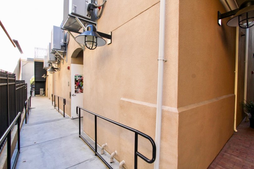 A pathway next to a peach color building with some AC equipment on the walls in MarketWalk, San Marcos, CA