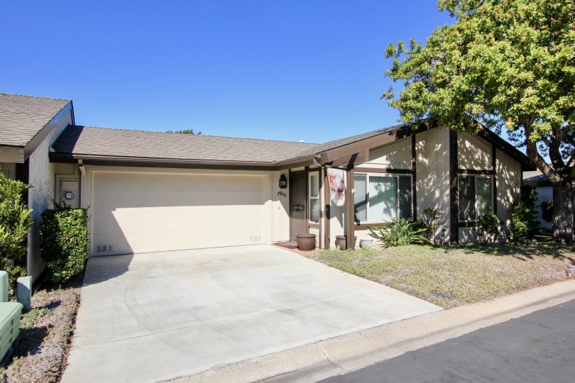 A house with a large driveway and garage door and a lawn with some bushes and a tree during a sunny day in Nob Hill, Vista, CA