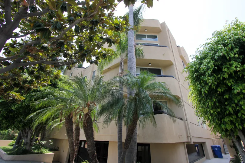 The corner of a four-story building on a sunny day in the Shenandoah Villas community of Beverly Center, California, depicting palm trees and foliage.