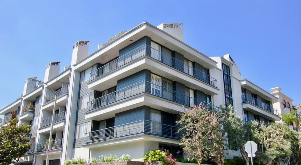 Four story Stucco Apartments at 1120 Granville with balconies and several trees and landscaping in Brentwood California