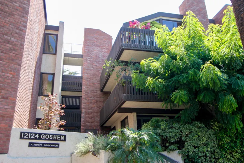A red brick building at 12124 Goshen with multiple balconies and a large tree