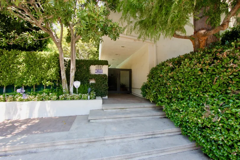A beautiful entrance with pretty good gate and lots of greenery including plants and trees. Colourfull flowers are adding life in the picture.