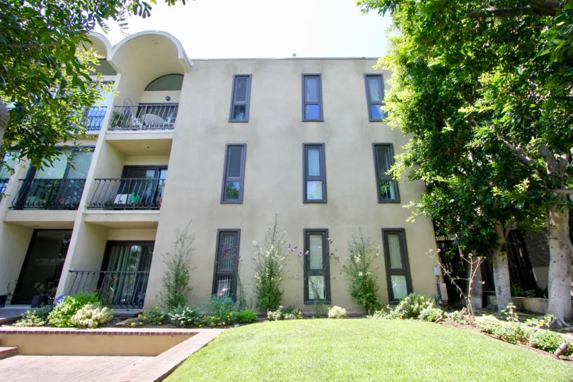 Outside view of three story building with well manicured lawn, lovely flowers and shrubs, and sunny balconies.