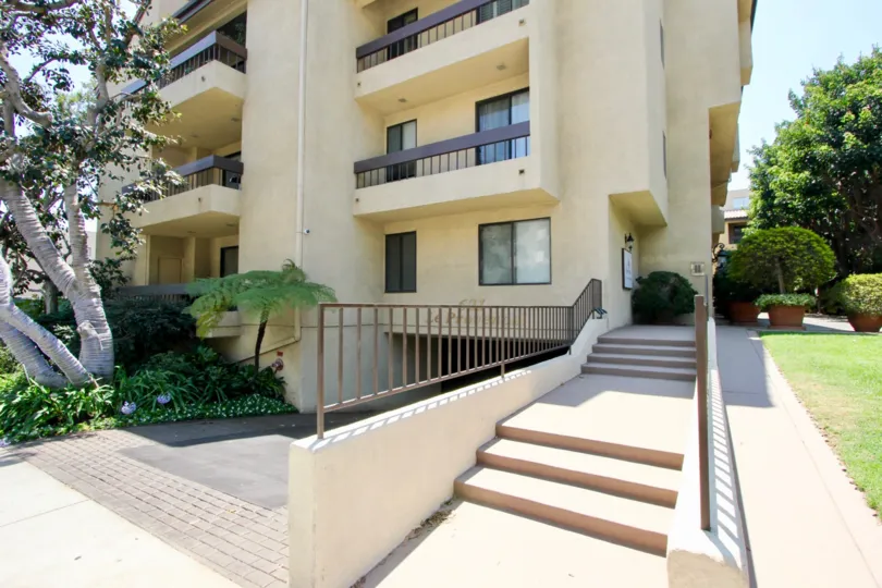 Side of apartment building at Le Provencal with stairs, entrance to parking, and manicured lawn and trees