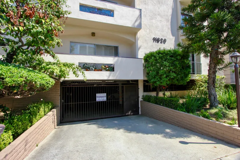 The entrance to an underground parking garage with trees and apartments