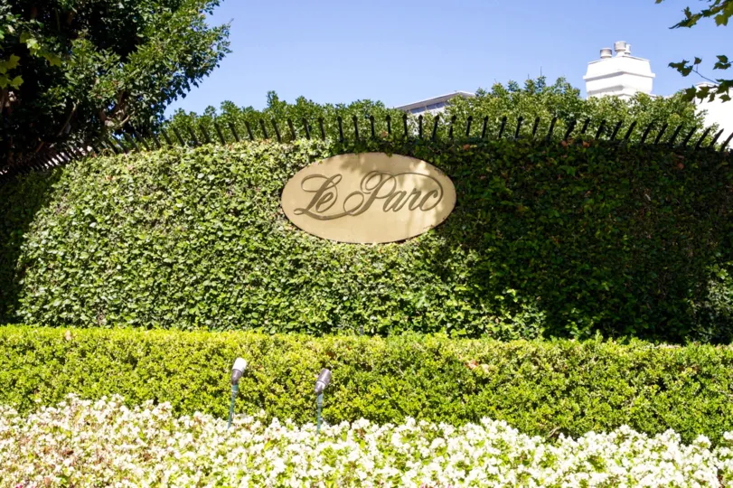 A gold plaque surround by shrubs on a fence display the name Le Parc