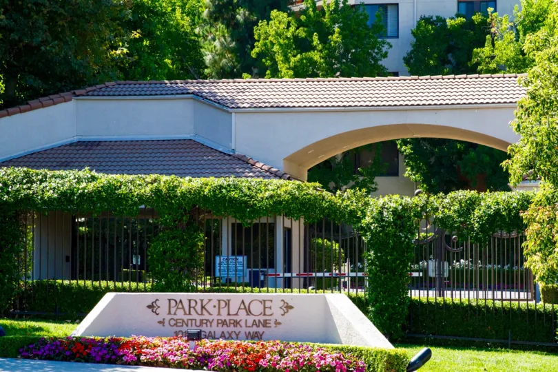 Gold letters on a small stucco structure surrounded by flowers showing Park Place name and address