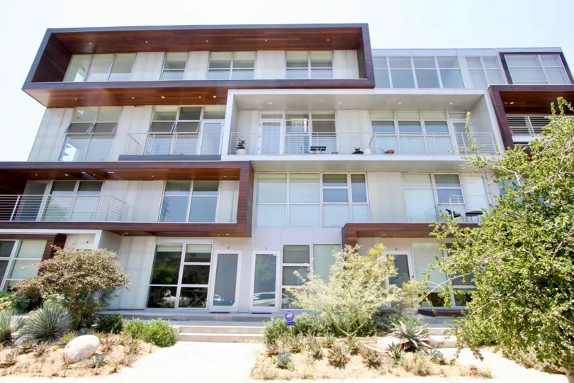 A sunny day in front of 611 Bronson in Hancock Park, California, with bushes, trees, and rocks