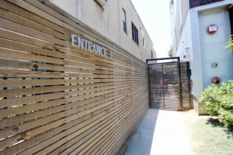 A wooden fence with a sign reading entrance pointing toward a wooden fence in an alley.