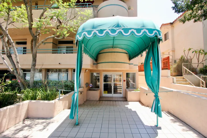 Entrance to Elmwood Regency with tile walk up, teal cover, pink building at trees.