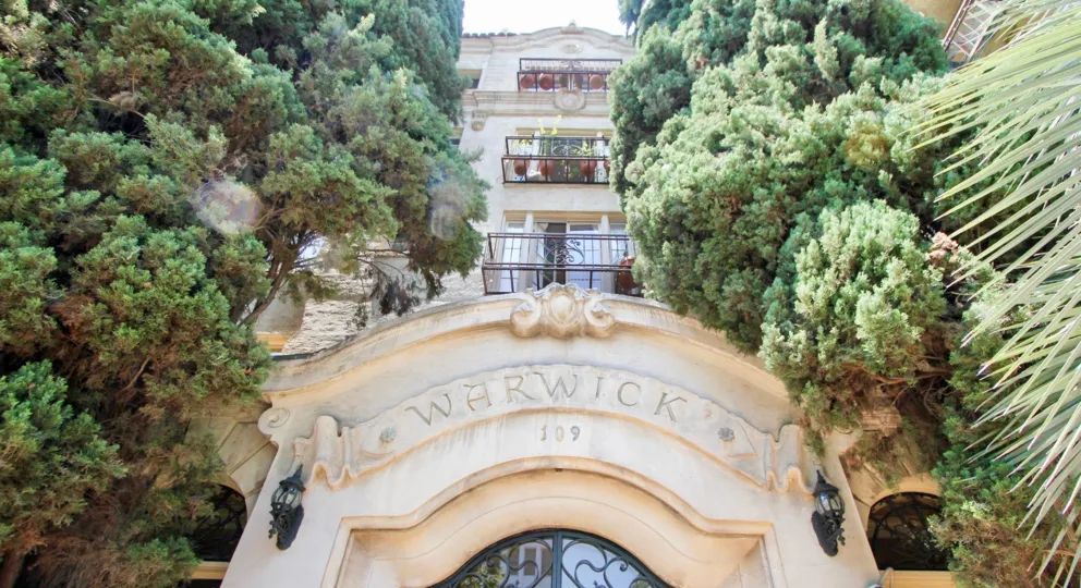 Front entrance at The Warwick. The entrance is arched with several all trees and 3 personal terraces above it.