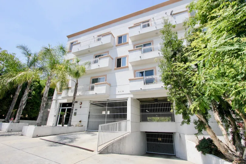 3-storey building with white walls and bars, with four palm trees adorning the entrance to the residence