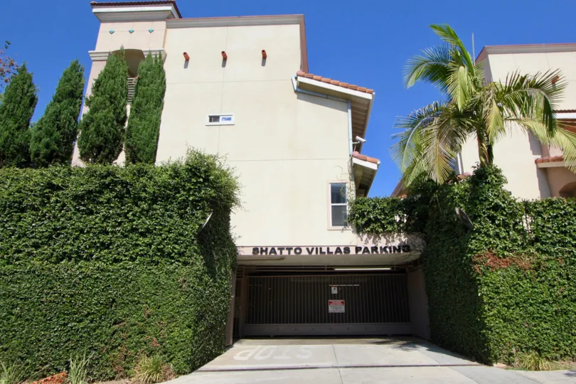 Shatto Villas Parking garage building surrounded by bushes and palm trees.