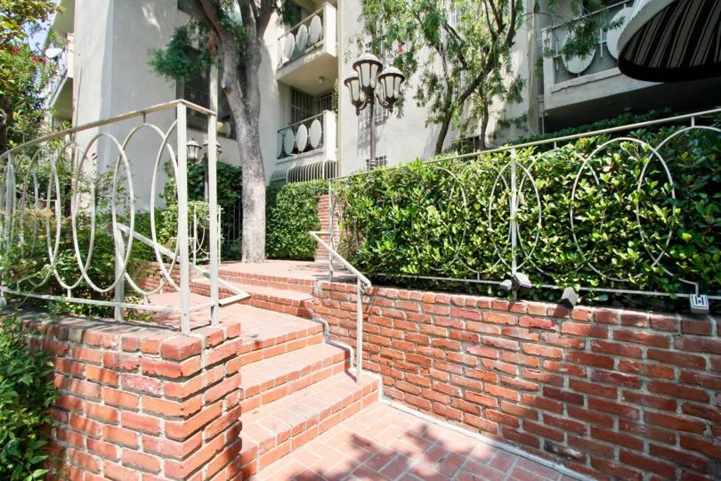 A red brick walkway leads up to The Fairmount. Shrubbery lines the walkway.