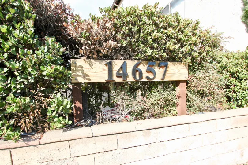 Wooden address sign nestled in shrubs set atop a stone retaining wall