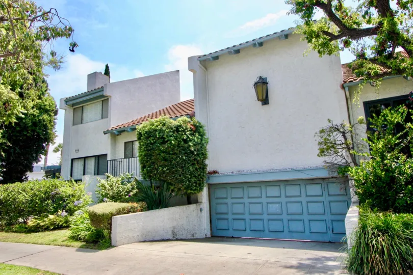 The front of a 1144 17th St building with a garage and bushes on a sunny day.