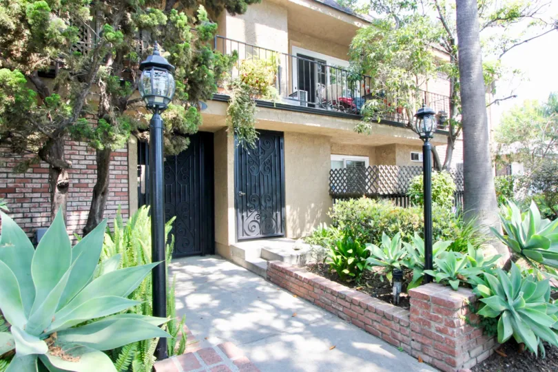 A HOUSE WITH BLACK DOOR AND WINDOWS SOME PLANTS ALSO IN FRONT OF THE HOUSE A BALCONY PLACE ALSO THERE