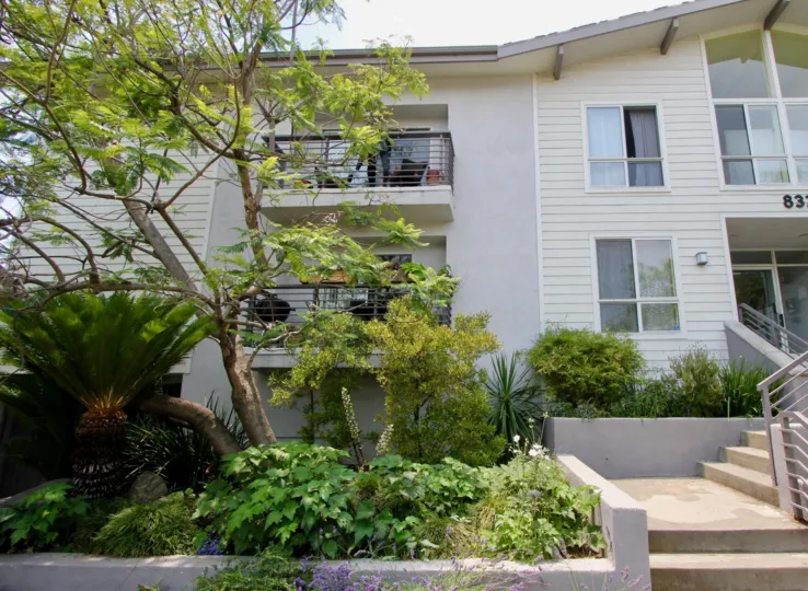 THE HOUSE WITH WHITE COLOUR TWO FLOORS WITH BALCONY AND SMALL WINDOWS AT THE MORNING WITH GREEN PLANTS