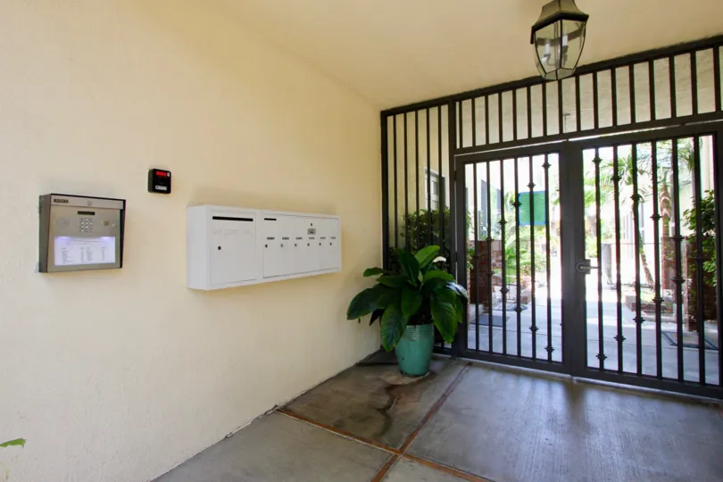 Entrance to courtyard secured with double wide iron gate, pleasant light peach color, bank of mail boxes and security intercom, fire alarm and overhead light.