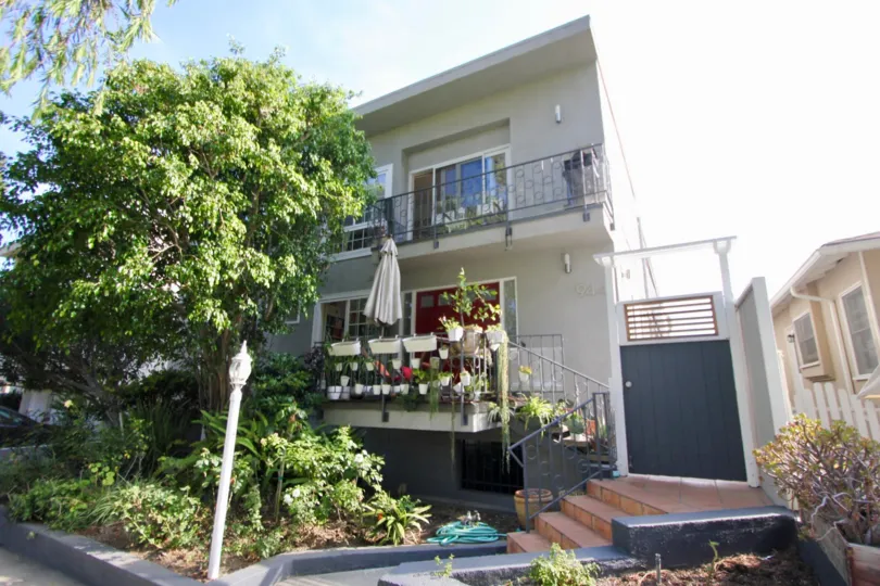 Two story building with brick steps up to secure entrance to back. Large tree and green garden, two balconies.