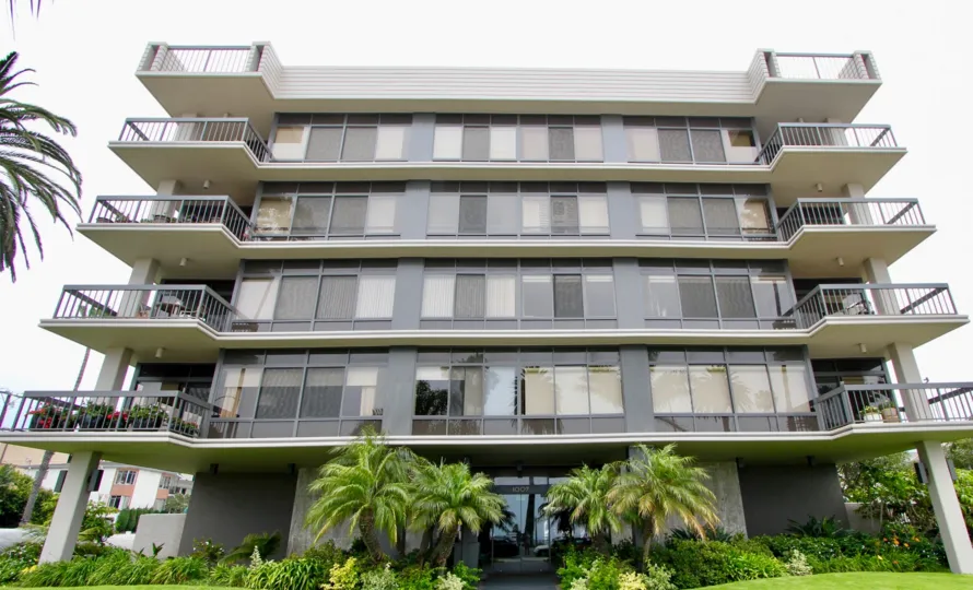 Large Boca Monica building with palm threes and bushes on a cloudy day.