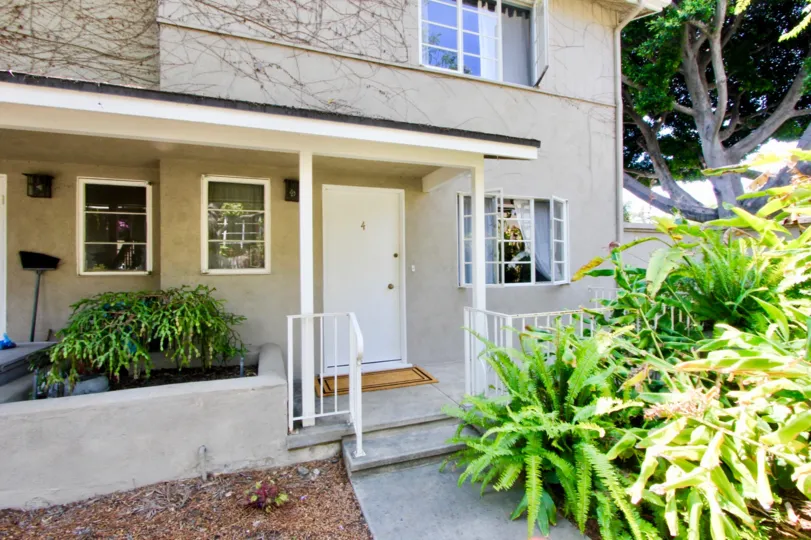 Front of concrete two-story house with lush, leafy greenery outside the doorstep.