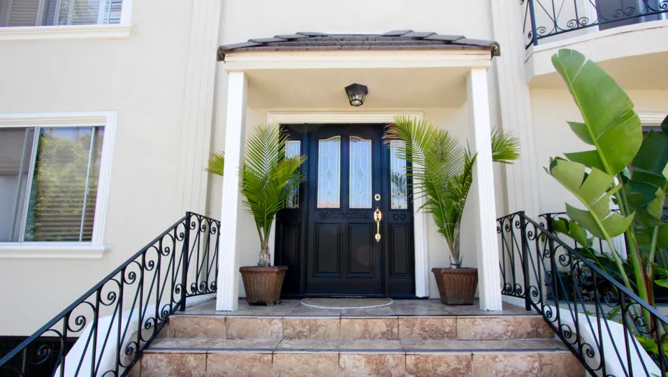 A white house in the Holloway House community with a black front door and green ferns