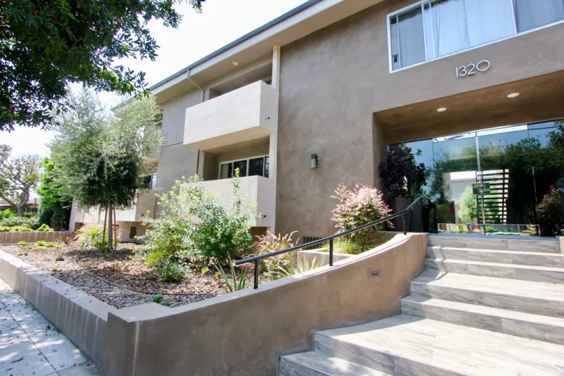 Glass entrance to a modern two story building with balconies on both floors and wide stairway leading to a sidewalk.