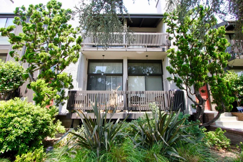 A tan house in The Pines community with lots of green plants in front and two balconies