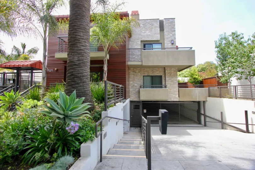 Multi-story building with balconies and garage with palm trees and landscaping