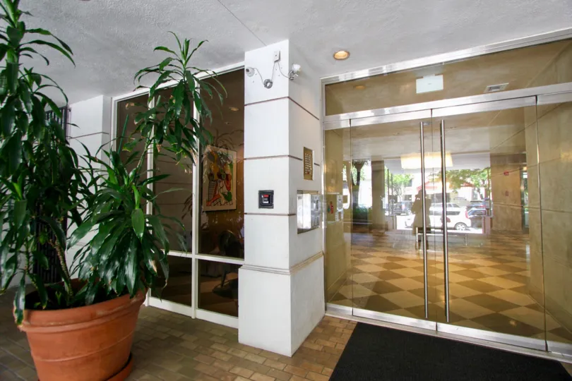 The fornt portion of a big apartment in the Wilshire Ocean Terrace with glass doors, windows and a small plant.