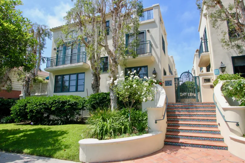 A white stone home surrounded by grass and trees with steps leading up in the Wilshire Princeton section of Santa Monica