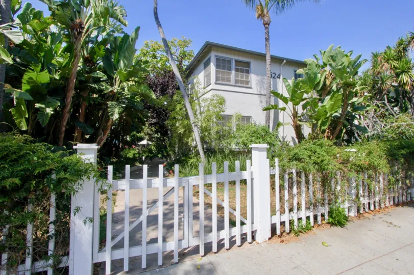 A white house in the Yale Street community with a white fence and many plants in the front yard
