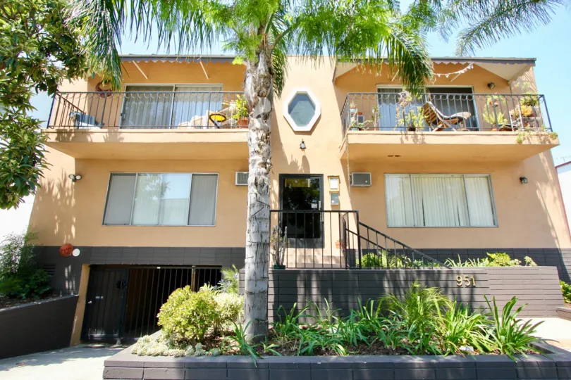 A yellow house in the Romaine Terrace neighborhood with two balconies and a large palm tree