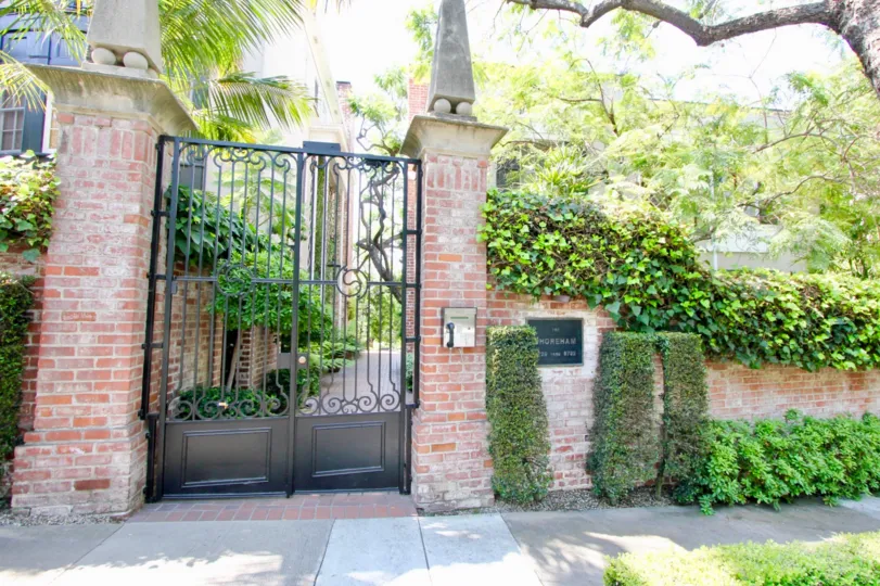 A red brick fence in The Shoreham neighborhood with a black gate and lots of green shrubs