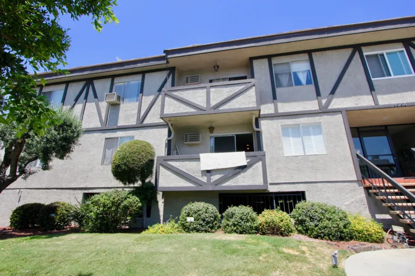 Sunny day at two story 1914 Corinth in West LA, California; front steps and door, towel hanging over first floor balcony. There are trees, grass, and bushes.