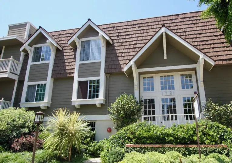 adorned gardens with shrubs and flowering bushes next to window house and too large roof