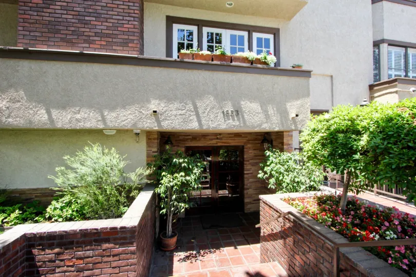Underway walkway made of brick with potted plants bring you inside below residential balconies