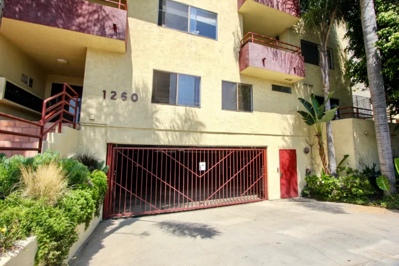 red parking garage gate next to tropical garden and grassy garden of entrance where mailboxes can be seen of the building