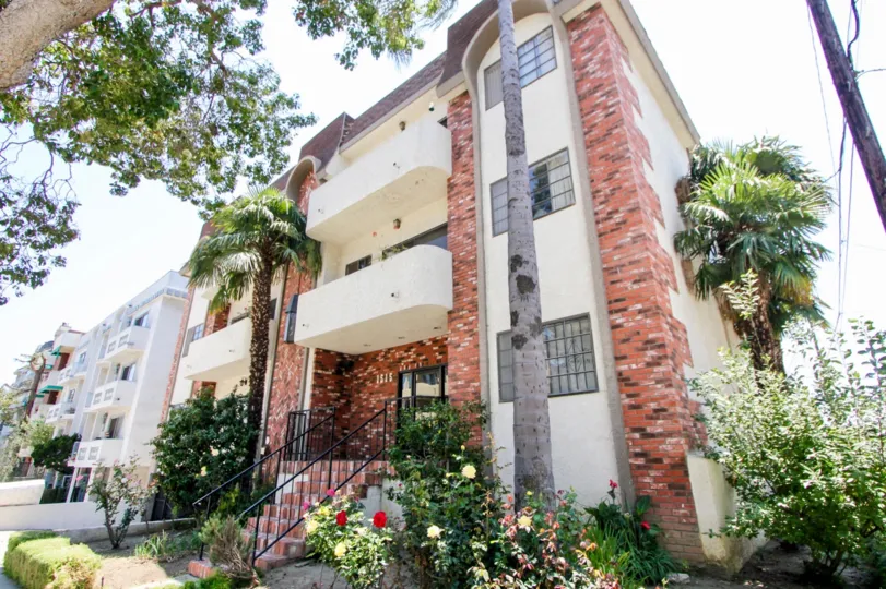 Beautiful flowers and Palm trees planted around a Cream colored brick decorated apartment building at Brighton Manor in West LA California