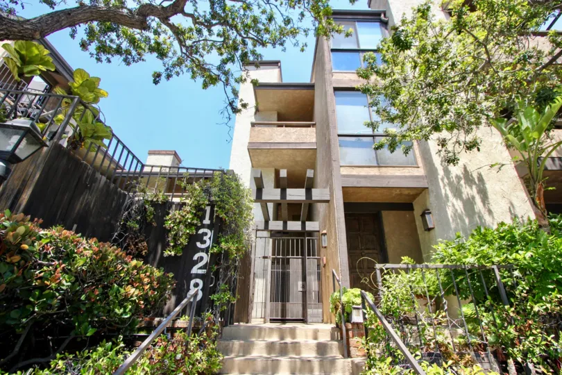 Modern building nestled inside gardens and large trees and a walk up entrance with a locked gate