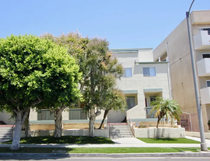 From the street you see some trees and grass and a palm tree in front of the townhouse