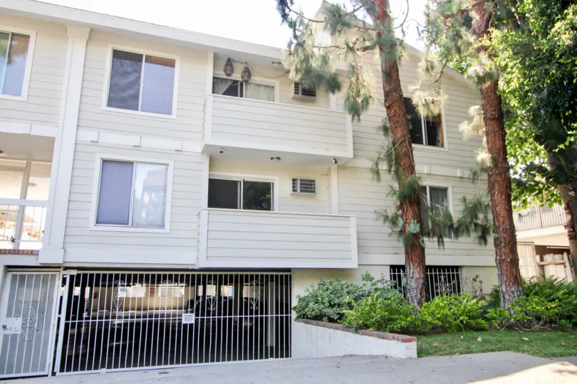 About 30 feet trees planted at the right side of A cream colored block of flats with gated underground parking at Granville Villas in West LA California