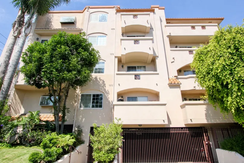 A 3 floors apartment complex with a parking entrance has palm trees around and tiles and spanish details