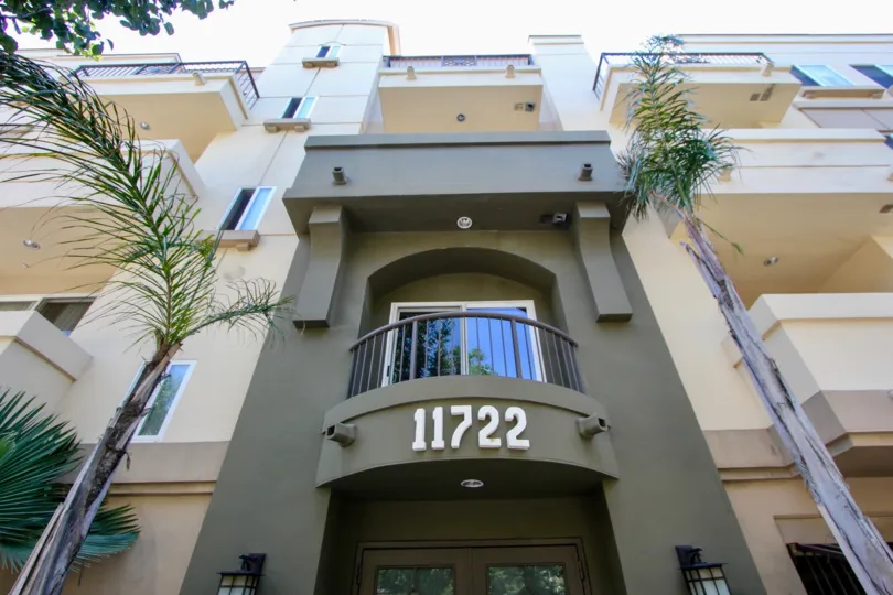 Front entrance to building with palm trees and gardens with balconies above