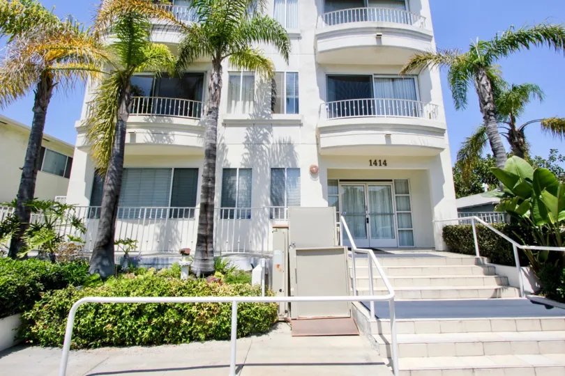 About 15 feet Palm trees plant all around a 2 story cream colored block of Flats at Saltair Regency in West LA California