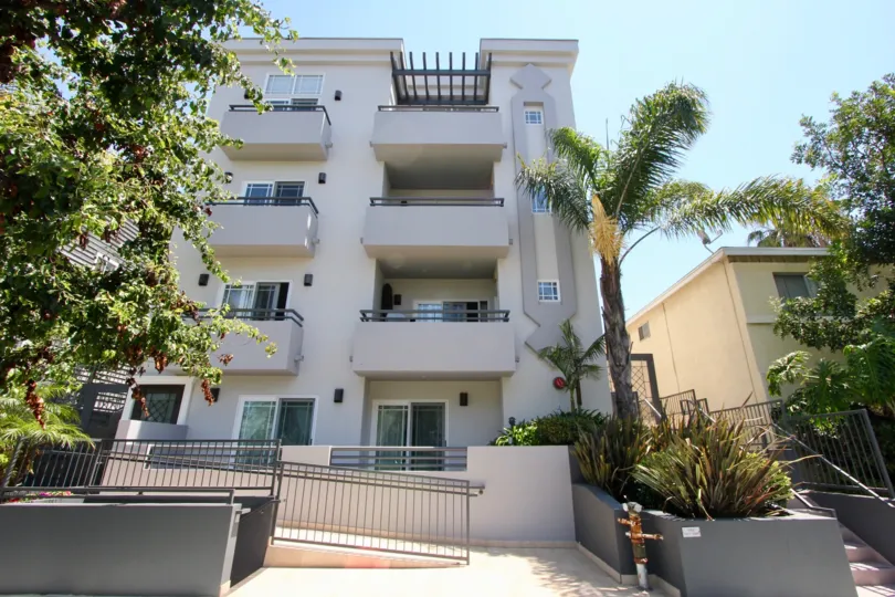 Hey apartment building surrounded by beautiful palm trees with a ramp staircase.