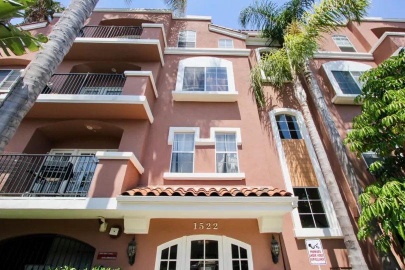 Palm trees planted in front of a 3 story Brown and Cream colored apartment building at Villa Rose in West LA California with house number 1522