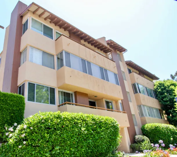 Three-story residence, with tall bushes and purple flowers at the entrance