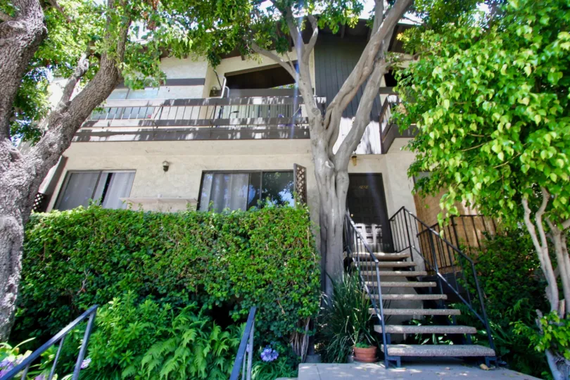 A house with stairs in 1818 kelton situated in the shadow of trees.